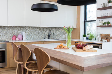 Example of a trendy l-shaped medium tone wood floor and brown floor kitchen design in Toronto with an undermount sink, flat-panel cabinets, white cabinets, stainless steel appliances, an island and white countertops