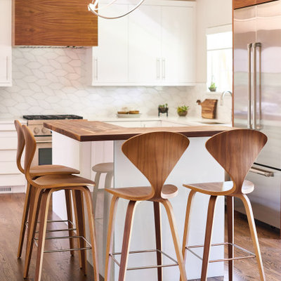 Example of a mid-sized trendy l-shaped medium tone wood floor and brown floor open concept kitchen design in Denver with an undermount sink, flat-panel cabinets, white cabinets, wood countertops, white backsplash, ceramic backsplash, stainless steel appliances, an island and brown countertops
