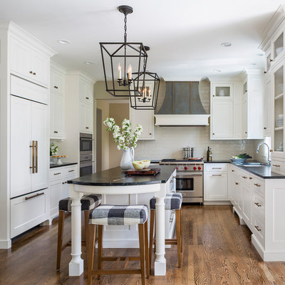 Mid-sized elegant medium tone wood floor and brown floor kitchen photo in Minneapolis with a single-bowl sink, recessed-panel cabinets, white cabinets, granite countertops, white backsplash, ceramic backsplash, stainless steel appliances, an island and black countertops