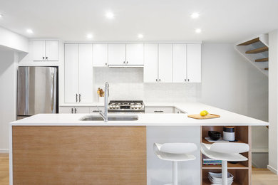 Foto på ett mellanstort funkis kök, med en undermonterad diskho, släta luckor, vita skåp, bänkskiva i kvarts, vitt stänkskydd, stänkskydd i stenkakel, rostfria vitvaror, ljust trägolv, en halv köksö och beiget golv