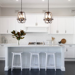 Design ideas for a mid-sized transitional galley kitchen in Sydney with recessed-panel cabinets, white cabinets, white splashback, subway tile splashback, stainless steel appliances, multiple islands, black floor and white benchtop.