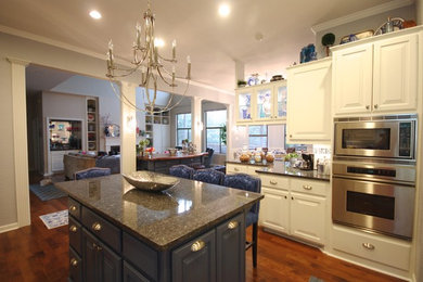 Example of a large ornate galley dark wood floor open concept kitchen design in Austin with an undermount sink, raised-panel cabinets, white cabinets, granite countertops, multicolored backsplash, stone tile backsplash, stainless steel appliances and two islands