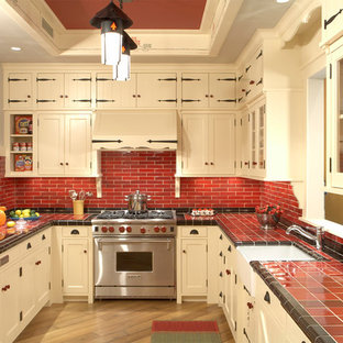 Foto de cocina en U, rústica, cerrada, con electrodomésticos de acero inoxidable, salpicadero rojo, encimera de azulejos, puertas de armario beige, armarios con paneles empotrados, fregadero sobremueble, salpicadero de azulejos de cerámica, suelo de madera en tonos medios, península y encimeras rojas