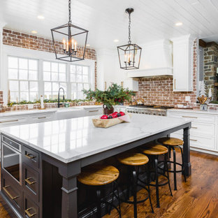 This is an example of a large traditional kitchen in DC Metro with a farmhouse sink, shaker cabinets, white cabinets, quartz benchtops, red splashback, brick splashback, stainless steel appliances, with island, white benchtop and medium hardwood floors.