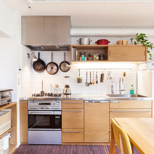 Inspiration for a mid-sized industrial single-wall open plan kitchen in Tokyo with an integrated sink, flat-panel cabinets, light wood cabinets, white splashback, subway tile splashback, white appliances, stainless steel benchtops, carpet and no island.