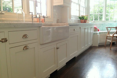 Example of a classic medium tone wood floor eat-in kitchen design in New York with a farmhouse sink, shaker cabinets, white cabinets, white backsplash, subway tile backsplash, paneled appliances and an island