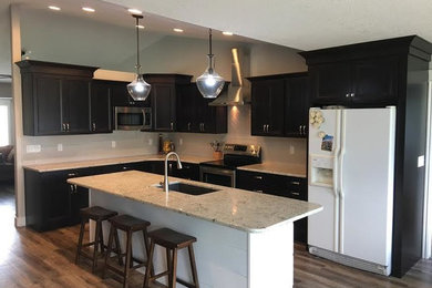 Mid-sized transitional l-shaped dark wood floor and brown floor open concept kitchen photo in Salt Lake City with an undermount sink, recessed-panel cabinets, brown cabinets, quartz countertops, beige backsplash, ceramic backsplash, stainless steel appliances and an island