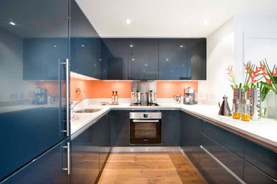 Photo of a medium sized contemporary u-shaped kitchen/diner in London with a submerged sink, flat-panel cabinets, blue cabinets, engineered stone countertops, orange splashback, glass sheet splashback, stainless steel appliances and no island.