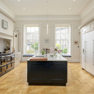 This is an example of a large transitional galley eat-in kitchen in Edinburgh with an integrated sink, shaker cabinets, blue cabinets, quartz benchtops, panelled appliances, light hardwood floors, with island, brown floor, grey benchtop, grey splashback and marble splashback.