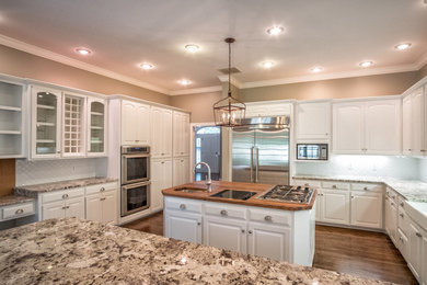 Inspiration for a large timeless u-shaped medium tone wood floor eat-in kitchen remodel in Other with a farmhouse sink, raised-panel cabinets, white cabinets, granite countertops, white backsplash, glass sheet backsplash, an island and stainless steel appliances