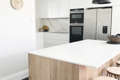 Modern inredning av ett mellanstort kök, med en undermonterad diskho, släta luckor, vita skåp, bänkskiva i kvarts, flerfärgad stänkskydd, stänkskydd i marmor, rostfria vitvaror, mörkt trägolv, en köksö och svart golv