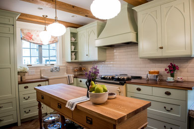Example of a farmhouse l-shaped porcelain tile enclosed kitchen design in Other with a farmhouse sink, recessed-panel cabinets, green cabinets, wood countertops, white backsplash, porcelain backsplash, colored appliances and an island