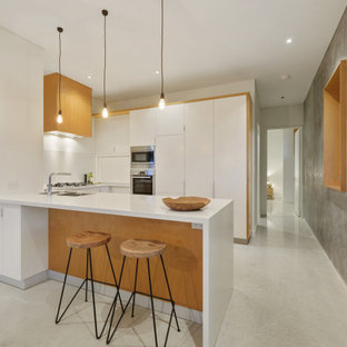 Photo of a midcentury u-shaped kitchen in Perth with a double-bowl sink, flat-panel cabinets, white cabinets, stainless steel appliances, concrete floors, a peninsula, grey floor and white benchtop.