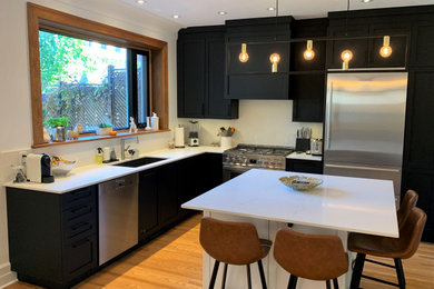Example of a trendy l-shaped medium tone wood floor kitchen design in Montreal with an undermount sink, shaker cabinets, black cabinets, quartzite countertops, white backsplash, stone slab backsplash, stainless steel appliances, an island and white countertops