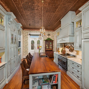 Photo of a victorian kitchen in Houston with a farmhouse sink, raised-panel cabinets, blue cabinets, wood benchtops, white splashback, subway tile splashback, black appliances, medium hardwood floors and with island.