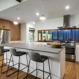Design ideas for a mid-sized modern galley kitchen pantry in Adelaide with a drop-in sink, flat-panel cabinets, white cabinets, concrete benchtops, metallic splashback, glass sheet splashback, stainless steel appliances, laminate floors, with island, brown floor and multi-coloured benchtop.