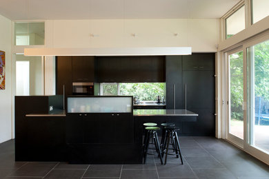 キャンベラにある中くらいなコンテンポラリースタイルのおしゃれなキッチン (フラットパネル扉のキャビネット、黒いキャビネット、ステンレスカウンター、黒いキッチンカウンター、一体型シンク、セラミックタイルの床) の写真