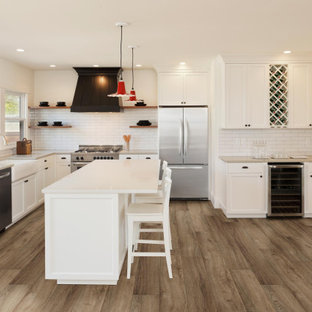 Photo of an expansive kitchen in Other with recessed-panel cabinets, white cabinets, white splashback, subway tile splashback, stainless steel appliances, vinyl floors, with island, brown floor and white benchtop.