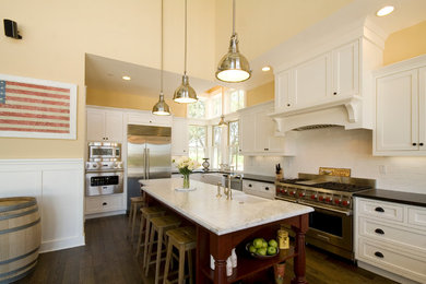 Example of a mid-sized country l-shaped dark wood floor eat-in kitchen design in San Francisco with a farmhouse sink, shaker cabinets, white cabinets, white backsplash, subway tile backsplash, stainless steel appliances and an island