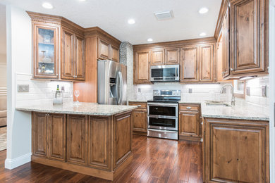 Example of a mid-sized classic l-shaped medium tone wood floor enclosed kitchen design in Orlando with an undermount sink, raised-panel cabinets, medium tone wood cabinets, quartz countertops, beige backsplash, porcelain backsplash, stainless steel appliances and a peninsula