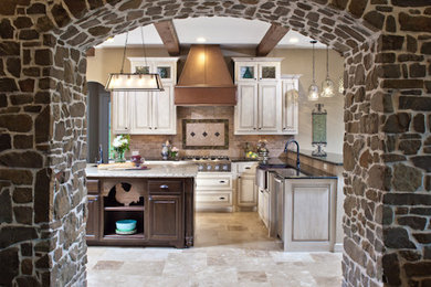 This is an example of a large rustic l-shaped enclosed kitchen in Other with a belfast sink, beige cabinets, beige splashback, stone tiled splashback, stainless steel appliances, granite worktops, travertine flooring and an island.