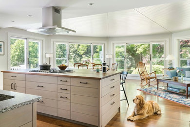 Example of a mid-sized farmhouse l-shaped medium tone wood floor and brown floor eat-in kitchen design in Boston with an undermount sink, flat-panel cabinets, light wood cabinets, wood countertops, white backsplash, stone tile backsplash, stainless steel appliances and an island