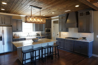Open concept kitchen - large rustic l-shaped dark wood floor and brown floor open concept kitchen idea in Birmingham with a farmhouse sink, raised-panel cabinets, gray cabinets, granite countertops, white backsplash, subway tile backsplash, stainless steel appliances and an island