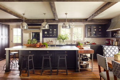 Example of a large cottage l-shaped brown floor eat-in kitchen design in New York with a farmhouse sink, black cabinets, white backsplash, subway tile backsplash, stainless steel appliances, an island, white countertops and shaker cabinets