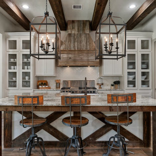 Mountain style l-shaped brown floor enclosed kitchen photo in Houston with a farmhouse sink, granite countertops, white backsplash, ceramic backsplash, stainless steel appliances, an island, glass-front cabinets, white cabinets and multicolored countertops