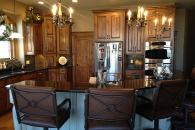 Example of a mid-sized mountain style single-wall medium tone wood floor and brown floor eat-in kitchen design in Other with raised-panel cabinets, light wood cabinets, granite countertops, stainless steel appliances and an island