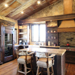 Mid-sized country u-shaped eat-in kitchen in Austin with a farmhouse sink, louvered cabinets, distressed cabinets, granite benchtops, multi-coloured splashback, stone tile splashback, panelled appliances, medium hardwood floors and with island.