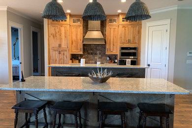 Large mountain style galley brown floor eat-in kitchen photo in Jacksonville with a farmhouse sink, recessed-panel cabinets, medium tone wood cabinets, granite countertops, gray backsplash, stone tile backsplash, stainless steel appliances, multicolored countertops and two islands