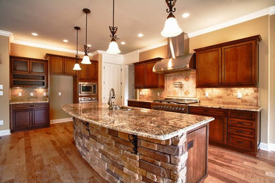 Mid-sized mountain style l-shaped medium tone wood floor and brown floor kitchen photo in Other with a double-bowl sink, raised-panel cabinets, medium tone wood cabinets, granite countertops, beige backsplash, stone tile backsplash, stainless steel appliances and an island