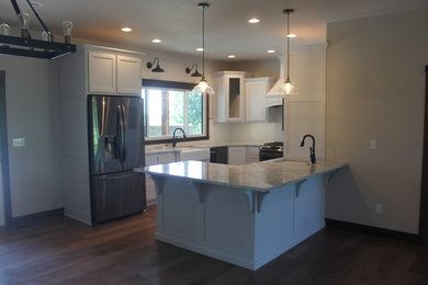 Example of a large transitional u-shaped laminate floor and beige floor enclosed kitchen design in Other with an undermount sink, raised-panel cabinets, white cabinets, quartzite countertops, white backsplash, ceramic backsplash, stainless steel appliances, an island and white countertops