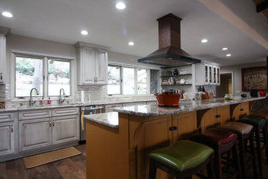 Large mountain style single-wall medium tone wood floor and brown floor open concept kitchen photo in Other with an undermount sink, raised-panel cabinets, distressed cabinets, granite countertops, multicolored backsplash, matchstick tile backsplash, stainless steel appliances, an island and multicolored countertops