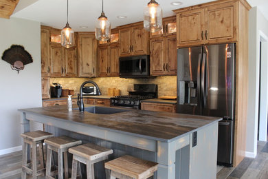 Mid-sized mountain style l-shaped ceramic tile and multicolored floor eat-in kitchen photo in Philadelphia with an undermount sink, raised-panel cabinets, medium tone wood cabinets, stone tile backsplash, black appliances, an island, stainless steel countertops and beige backsplash