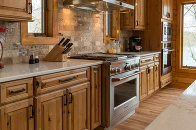Mountain style light wood floor open concept kitchen photo in Milwaukee with an undermount sink, raised-panel cabinets, medium tone wood cabinets, quartzite countertops, stainless steel appliances and an island