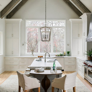 Immagine di una cucina country con lavello stile country, ante con riquadro incassato, ante bianche, paraspruzzi bianco, paraspruzzi a finestra, elettrodomestici in acciaio inossidabile, pavimento in legno massello medio, pavimento marrone, top bianco e top in quarzo composito