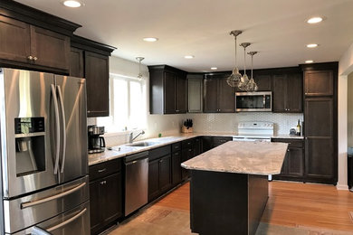 Example of a mid-sized transitional l-shaped eat-in kitchen design in New York with a single-bowl sink, recessed-panel cabinets, dark wood cabinets, quartz countertops, white backsplash, ceramic backsplash, stainless steel appliances and an island