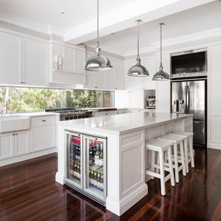 This is an example of a mid-sized transitional l-shaped eat-in kitchen in Perth with shaker cabinets, white cabinets, quartz benchtops, white splashback, window splashback, stainless steel appliances, with island, a farmhouse sink, dark hardwood floors and brown floor.