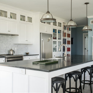 Immagine di un ampio cucina con isola centrale stile americano con lavello integrato, ante con riquadro incassato, ante bianche, top in superficie solida, paraspruzzi bianco, paraspruzzi con piastrelle in pietra, elettrodomestici in acciaio inossidabile e pavimento con piastrelle in ceramica