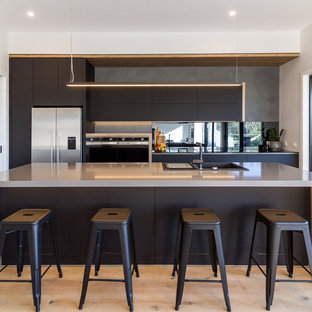 Design ideas for a mid-sized industrial galley kitchen in Melbourne with a drop-in sink, flat-panel cabinets, black cabinets, quartz benchtops, black splashback, mirror splashback, stainless steel appliances, light hardwood floors, beige floor, grey benchtop and a peninsula.
