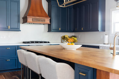 Example of a mid-sized transitional u-shaped medium tone wood floor open concept kitchen design in Sacramento with a farmhouse sink, recessed-panel cabinets, blue cabinets, quartz countertops, white backsplash, stone slab backsplash, black appliances, an island and white countertops