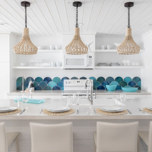 Photo of a small beach style galley eat-in kitchen in Tampa with a drop-in sink, flat-panel cabinets, white cabinets, laminate benchtops, blue splashback, mosaic tile splashback, stainless steel appliances, ceramic floors, with island, white floor, white benchtop and wood.