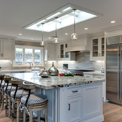 Large transitional l-shaped light wood floor and beige floor eat-in kitchen photo in Orange County with white cabinets, solid surface countertops, gray backsplash, stone tile backsplash, stainless steel appliances, a farmhouse sink, an island and recessed-panel cabinets
