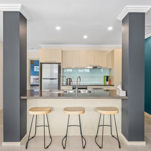 Small beach style galley kitchen in Melbourne with quartz benchtops, with island, a drop-in sink, flat-panel cabinets, beige cabinets, blue splashback, glass sheet splashback, stainless steel appliances, beige floor and brown benchtop.