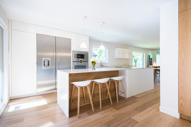 Large trendy single-wall medium tone wood floor and brown floor eat-in kitchen photo in Montreal with an island, an undermount sink, flat-panel cabinets, white cabinets, quartz countertops, white backsplash, ceramic backsplash and stainless steel appliances