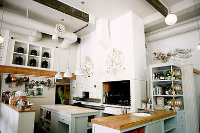Exempel på ett mellanstort industriellt kök, med en nedsänkt diskho, släta luckor, blå skåp, träbänkskiva, vitt stänkskydd, stänkskydd i tegel, rostfria vitvaror, mörkt trägolv, en köksö och svart golv