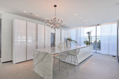 Example of a mid-sized trendy single-wall concrete floor kitchen design in Miami with flat-panel cabinets, white cabinets, marble countertops, paneled appliances and an island