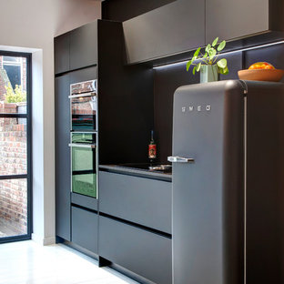 This is an example of a small contemporary galley kitchen in Other with flat-panel cabinets, black cabinets, quartzite benchtops, black splashback, glass sheet splashback, black appliances, painted wood floors, no island, white floor and black benchtop.